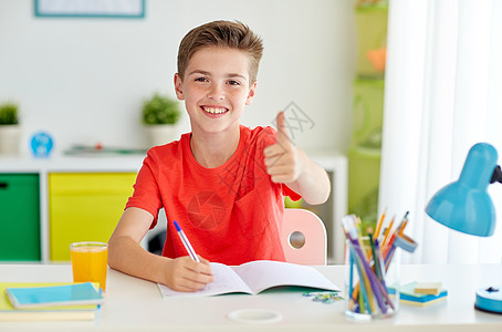 教育童人的快乐的学生男孩家里写笔记本,竖大拇指快乐的学生男孩家里写笔记本图片