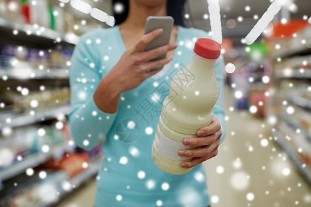 销售,购物,消费主义人的轻的女客户与智能手机持奶瓶杂货店超市雪上顾客超市智能手机牛奶图片