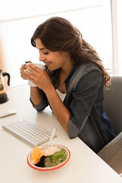 轻的女人电脑桌上吃早餐图片