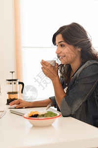 轻的女人电脑桌上吃早餐图片