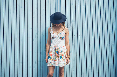 个穿着夏装戴着帽子的轻女人站外的蓝色篱笆旁图片