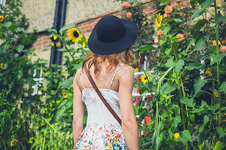 个轻的女人戴着顶帽子件连衣裙,夏天个阳光明媚的日子里,房子外欣赏些向日葵图片