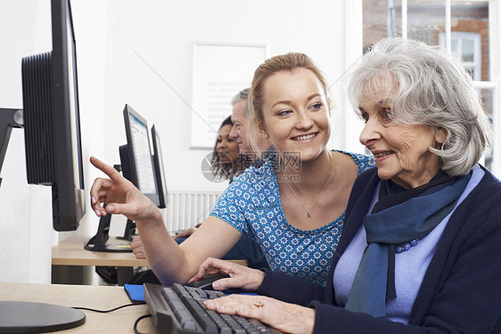 辅导老师帮助老年女子上电脑课图片