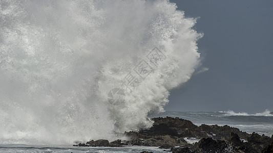 股巨大的波浪风暴河口的海岸线上撞击岩石,造成了巨大的飞溅图片