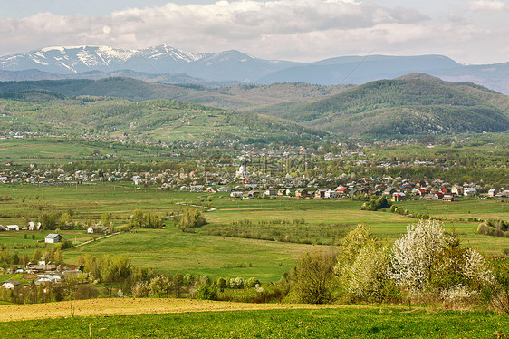 阳光明媚的春天村庄城镇的山麓背景上的山脉阳光明媚的绿色春天景观图片