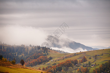 山的秋天景观与五颜六色的森林背景上云雾缭绕的山山上的村庄图片