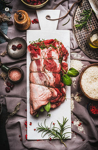 生羊肉肩烤与绳子,充满草药香料白色大理石切割板准备乡村背景与餐巾,米饭烹饪勺子,顶部视图肉类食品图片