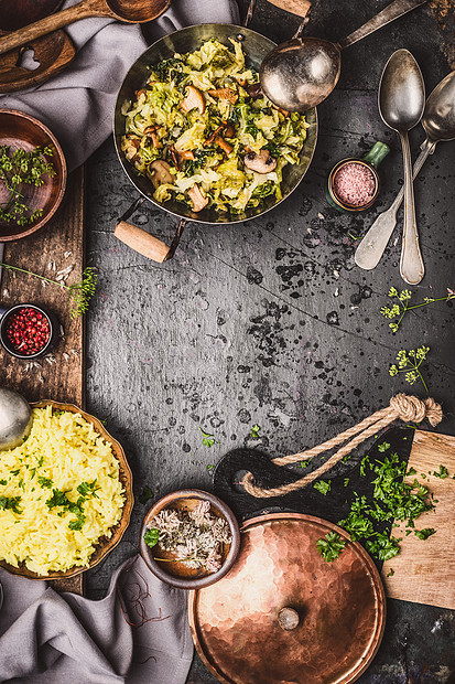 素食菜肴与黄米,卷心菜蘑菇烹饪锅上的黑暗乡村厨房桌子与勺子,顶部视图,框架图片