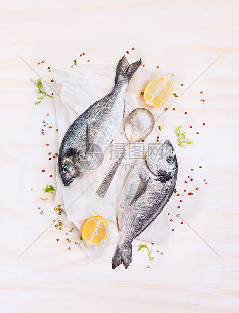 两条生的多拉多鱼,柠檬,香料勺子纸上,构成白色的木制背景,顶部的景色图片