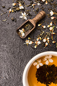 几个胖女人茉莉花茶与木勺,杯子新鲜的花黑色的石头背景,顶部查看背景