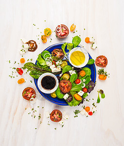 新鲜沙拉与番茄,费塔奶酪,香醋油蓝色盘子白色木制背景,顶部的图片