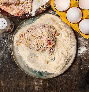生肉Schnitzel准备盘子与粉,鸡蛋包屑木制背景,顶部视图,图片