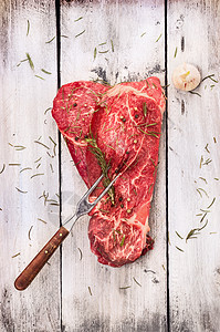 生牛肉与肉叉旧的白色灰色木制背景,顶部视图图片