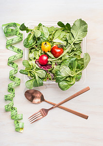 健身节食沙拉与餐具测量磁带白色木制背景,顶部视图混合蔬菜沙拉碗健康午餐图片