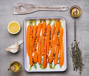 烤胡萝卜加绿色香草,大蒜,柠檬蜂蜜灰色混凝土背景,顶部视图,平躺健康干净的食物素食烹饪饮食观念图片