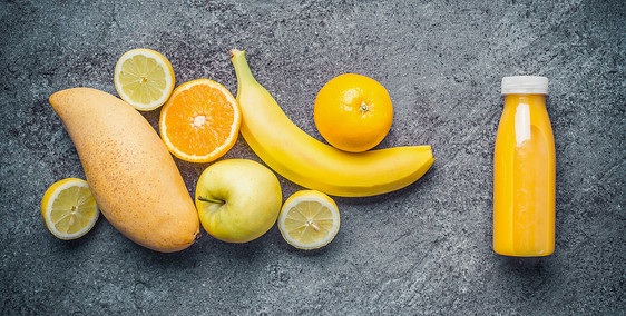 自制健康清爽的水果饮料瓶中加入配料黄色柑橘水果冰沙,多汁的维生素饮料灰色混凝土背景,顶部查看食物图片