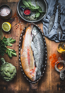 鱼盘烹饪准备两条鳟鱼以烘焙的形式出现木制乡村厨房桌子的背景上,蔬菜调味品的成分,风景背景图片