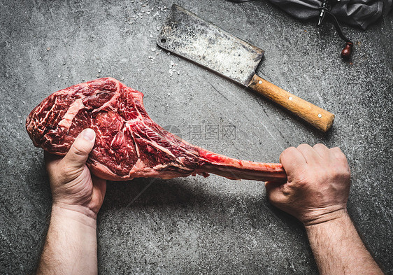 生战斧牛肉牛排男手中与肉刀黑暗的乡村背景屠夫手着战斧牛排,俯视图图片