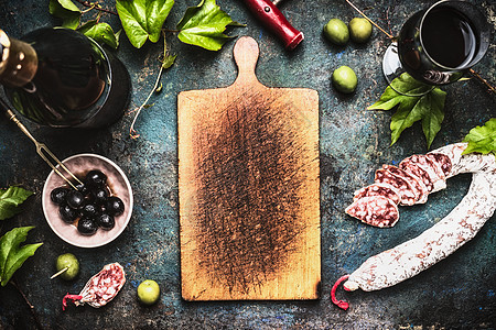 意大利食品背景与葡萄酒,橄榄香肠周围的木制切割板,顶部视图图片