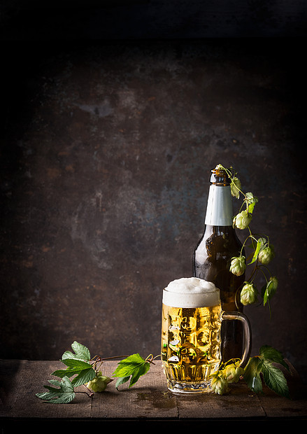 璃瓶啤酒杯与泡沫帽啤酒花桌子上黑暗的乡村背景,正的,静物图片