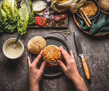 女手自制美味汉堡与鸡肉乡村厨房桌子背景与配料,顶部的视野图片