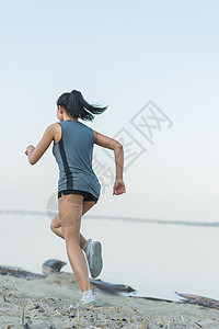 轻的女士早上海滩上跑步图片