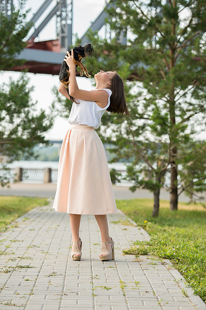 美丽的轻女人穿着优雅的连衣裙,抱着小狗,夏天的公园散步图片