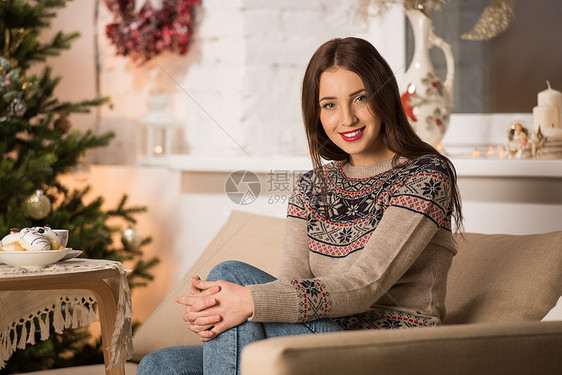 穿着冬装的漂亮女人坐诞树附近的沙发上图片
