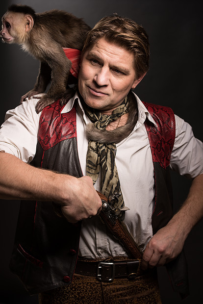 成熟的男人冒险家穿着旅行者的服装,他的猴子同伴着黑色背景的旧