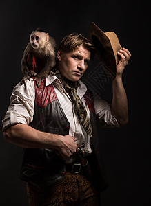 卷尾猴成熟的男人冒险家穿着旅行者的服装,他的猴子同伴着黑色背景的