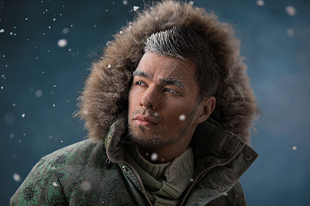 冬天的雪中,英俊的男人穿着带毛皮帽的夹克图片