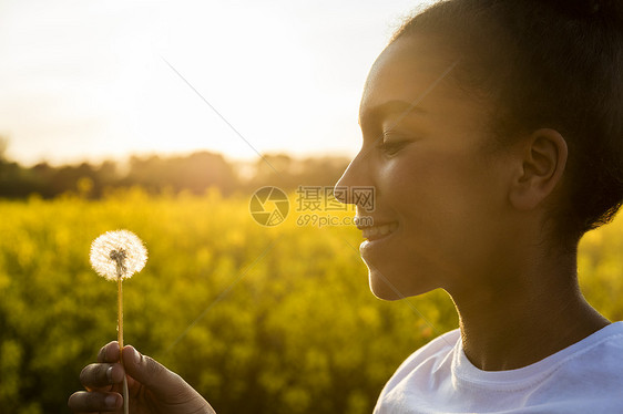 户外肖像美丽的快乐混合种族非裔美国女孩十几岁的女轻女子微笑金色的夕阳灯光蒲公英时钟花图片