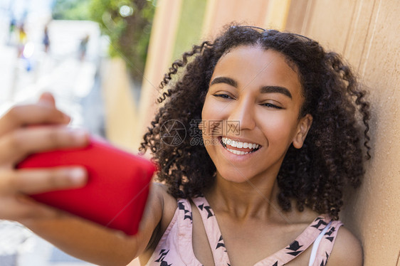 美丽快乐的混合种族非裔美国女孩十几岁的女孩子笑着用完美的牙齿拍自拍照片与手机图片