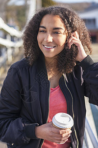 美丽快乐的混合种族非裔美国女孩十几岁的女青,微笑着喝着外卖咖啡,外穿着黑色轰炸机夹克图片
