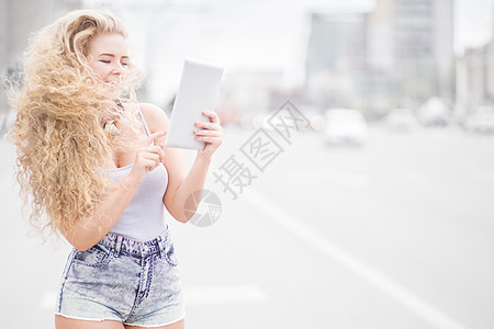 快乐的轻女人,脖子上戴着老式音乐耳机,平板电脑上上网,城市背景下摆姿势图片