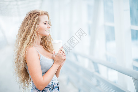 美丽的轻女人,留着长长的卷发,着个走的咖啡杯,站城市背景的桥上图片