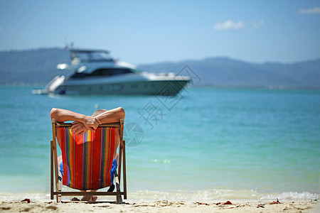 躺椅上的人男人海滩上的躺椅上放松,看着游艇图片