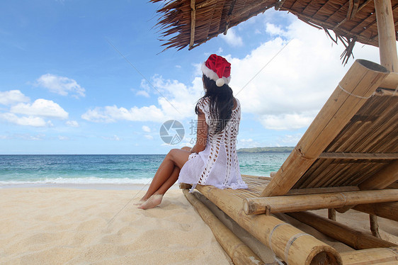 坐躺椅上的女人菲律宾白色沙滩上,位戴着诞老人帽子的女士坐躺椅上,着草伞图片