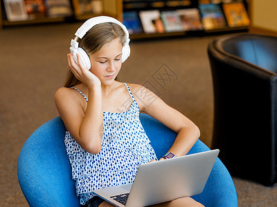 个带耳机的十几岁女孩坐图书馆里阅读倾听图片