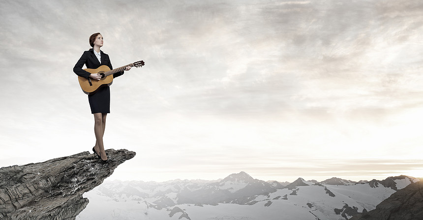 女商人弹声吉他开朗的女商人站岩石边缘弹吉他