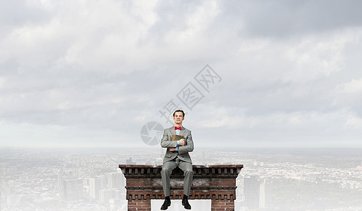 书呆子轻的商人戴着红蝴蝶结,手着书坐建筑顶部图片
