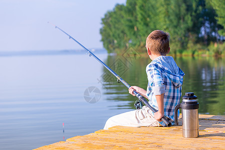 穿着蓝色衬衫的男孩坐海边的码头上,着鱼竿图片