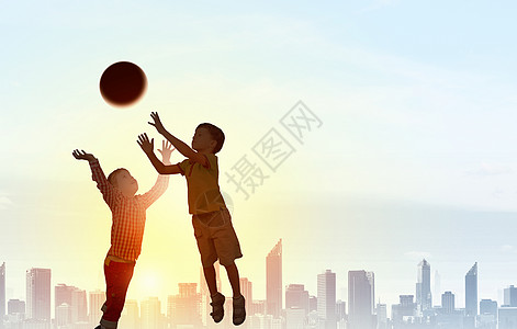 快乐粗心的童日落的背景下,孩子们跳着接球的剪影图片