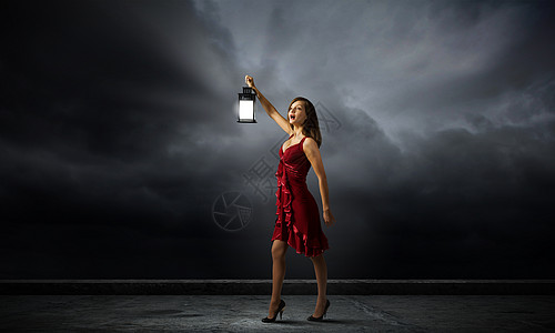 为了寻找什么轻迷人的女人穿着红色连衣裙,提着灯笼黑暗中行走图片