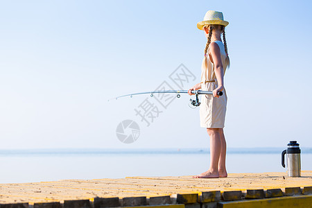 穿着连衣裙帽子的女孩带着钓鱼竿码头钓鱼图片