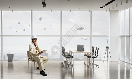 用平板设备的商人穿着白色西装的优雅商人坐办公室椅子上图片