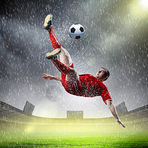 足球运动员击球足球运动员穿着红色衬衫雨中体育场击球图片