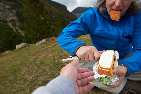 徒步旅行的人野餐时切片美味的奶酪,并与朋友分享图片