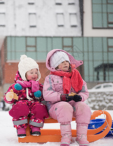 两个可爱的小女孩下雪的冬天坐户外雪橇上,休息时吃美味的饼干的肖像图片