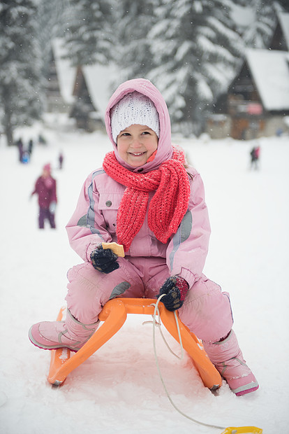 可爱的小女孩的肖像,坐雪橇冬季与新鲜的雪,吃饼干休息图片